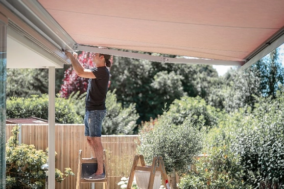 Person befestigt eine ausgefahrene Markise auf einer Leiter.
